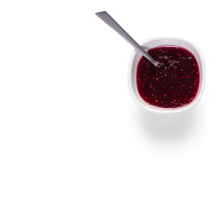 Raspberries jam in a white bowl with a teaspoon on a white background isolationの写真素材