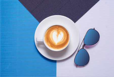 Cup of coffee cappuccino sunglasses on a colorful blue white backgroundの写真素材