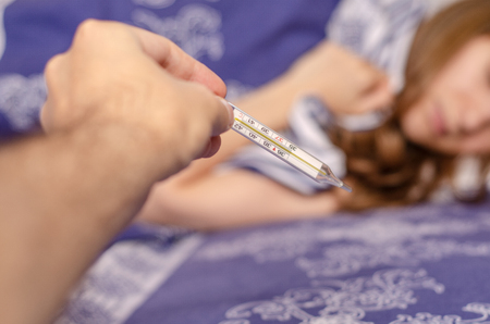 Woman lies in bed looking at thermometer sick pain virusの写真素材