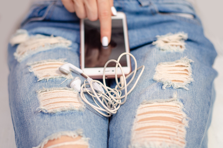 Woman in jeans looks at mobile phone smartphone and headphones touch device fashion beautyの写真素材