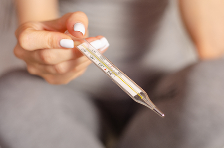 Woman sits ill in the hands of a thermometer virus flu sickの写真素材