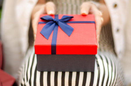 A woman is holding a gift box in hand on blur background