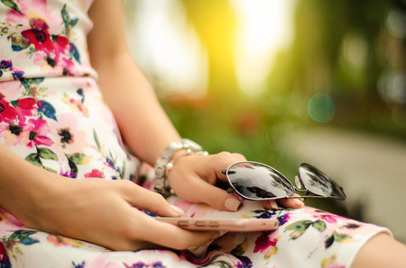Beautiful woman in dress with sunglasses and mobile phone smartphone in hands summer vacations journey trip blur nature backgroundの写真素材