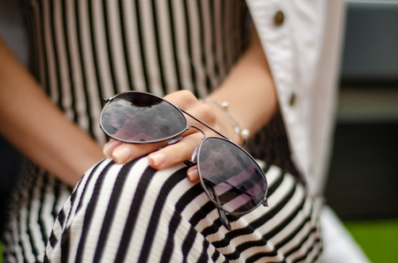 A woman is sitting on a bench with sunglasses in hands sun nature on blur backgroundの写真素材