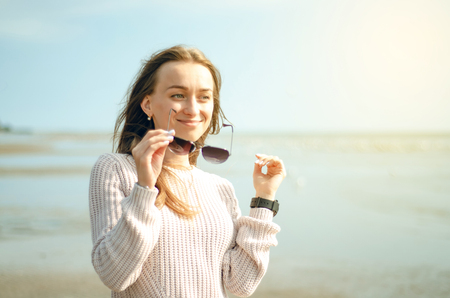 Woman holds sunglasses on the background of the sea sun sweater watch autumn coldの写真素材