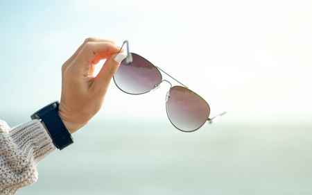 Female hand holds sunglasses on the background of the sea sun sweater watch autumn coldの写真素材