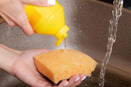 Sponge for washing dishes. detergent in hands with washing kitchen faucet waterの写真素材