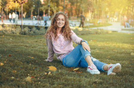 Beautiful woman in jeans and a sweatshirt in the street sneakers autumn park smiling happy blur backgroundの写真素材