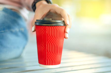 Beautiful woman in jeans and a sweatshirt with coffee in the street blur backroundの写真素材