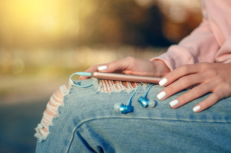Woman sitting jeans sweatshirt watch smartphone mobile phone headphones on city street blur backroundの写真素材