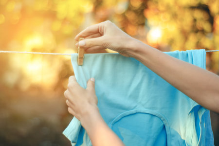 Blue green T-shirt hanging on a clothespin female hand nature on blur background