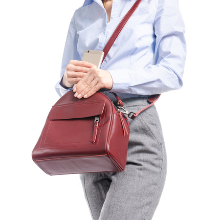 Woman in gray pants and blue shirt put smartphone in red bag macro isolated on white background.の写真素材