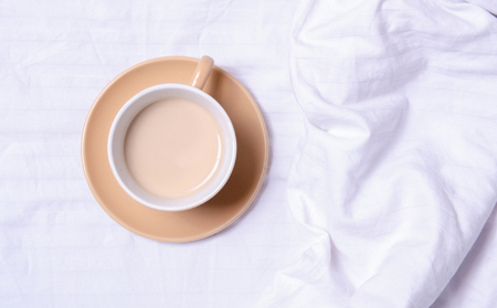 Cup of coffee on the white linens bed, top viewの写真素材