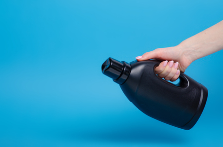 Black bottle laundry gel in hand on blue background isolationの写真素材
