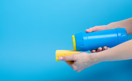 Blue bottle detergent powder clean sponge in hand on blue backgroundの写真素材
