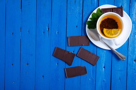 White cup of mint tea with lemon and chocolate on a blue wooden background, top view, empty spaceの写真素材
