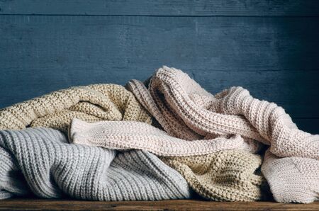 Pile of knitted warm clothes on wooden background, sweaters, knitwearの写真素材