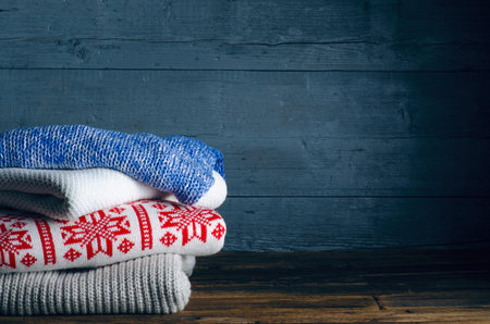 Pile stack folded of knitted winter clothes on wooden background, sweaters, knitwear