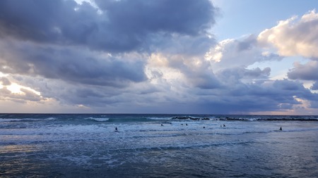 Group of surfers silhouetted with colourful evening sky and sea background, Mediterranean seacoast, Haifa, Israelの写真素材