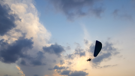 Silhouette of a male paraglider on a paraplan against a background of a sunset in the sky and clouds hovering over the sea. Concept: freedom, loneliness, hobby, sport.の写真素材