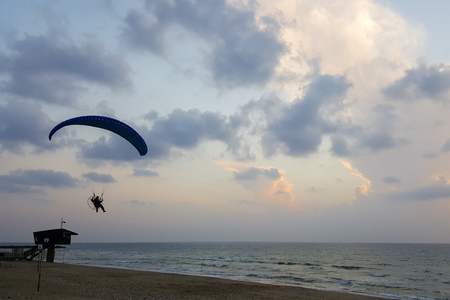 Silhouette of a male paraglider on a paraplan against a background of a sunset in the sky and clouds hovering over the sea. Concept: freedom, loneliness, hobby, sport.の写真素材