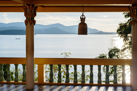 Terrace with columns, Buddhist bell, view of the sea and mountains in the distance. The rays of the pre-dawn sun are reflected in the water. Thailand.の写真素材