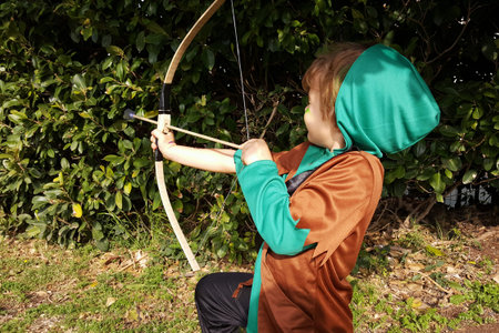 Boy playing outdoors with a bow, aiming with one eye shut. Dressed for Purim party