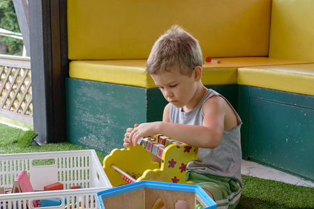 Handsome pre-school boy in T-shirt enthusiastically plays toys in playroomの写真素材