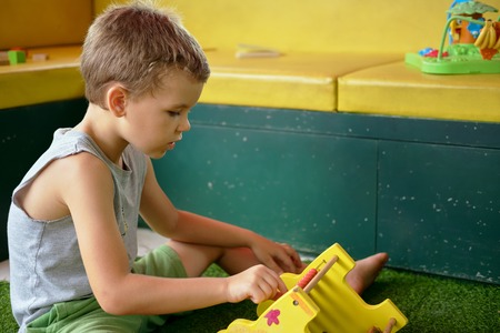 Handsome pre-school boy in T-shirt enthusiastically plays toys in playroomの写真素材