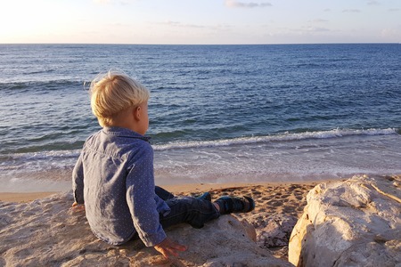 Boy sitting on rocks near sea shore waiting. Haifa beach. Israelの写真素材