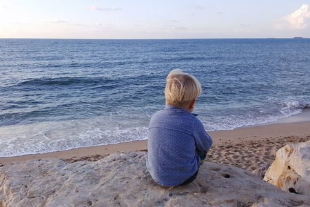 Boy sitting on rocks near sea shore waiting. Haifa beach. Israelの写真素材