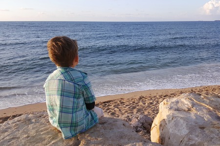 Boy sitting on rocks near sea shore waiting. Haifa beach. Israelの写真素材