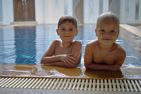 Two cute brothers preschool age, wet blonde hair, at the pool edge. Looking into cameraの写真素材