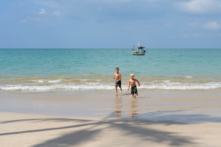 Two brothers boys playing on beach, run away from waves. Beautiful sunny day. Khao Lak, Thailand. Concept vacation, holidays, familyの写真素材