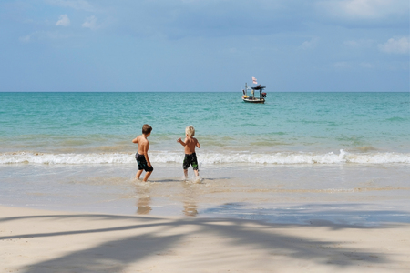 Two brothers boys playing on beach, run away from waves. Beautiful sunny day. Khao Lak, Thailand. Concept vacation, holidays, familyの写真素材