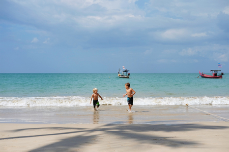 Two brothers playing on beach, run away from waves. Beautiful sunny day, Thailand. Concept: vacation, familyの写真素材
