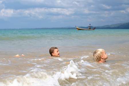 Two boys play in waves of surf, Thailand. Concept: family vacationの写真素材