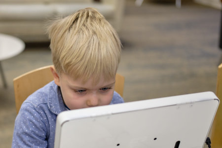 Elementary school boy sitting in library, using touchscreen computer for education