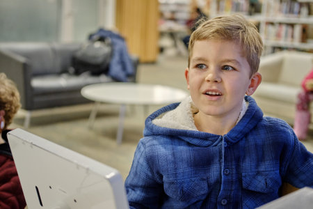 Elementary school boy sitting in library, using touchscreen computer for education