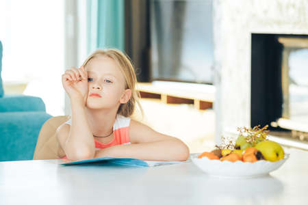little girl at the table with a notebook, doing homework.の写真素材