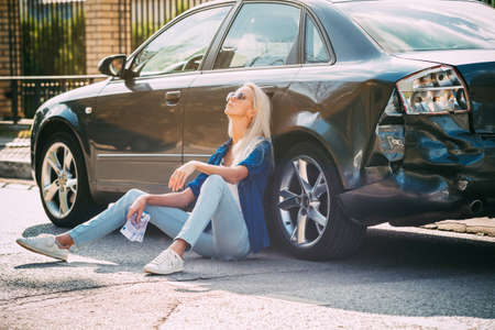 The girl sits at the broken car with money bills for repair.の写真素材