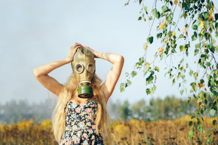 A girl in a dress walking in nature wears a gas mask. The concept of environmental pollution,...