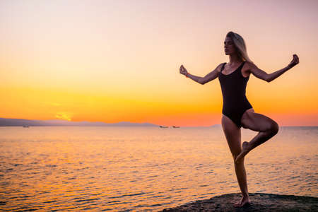 A girl on the beach at dawn doing yoga. The concept of a healthy lifestyle.の写真素材