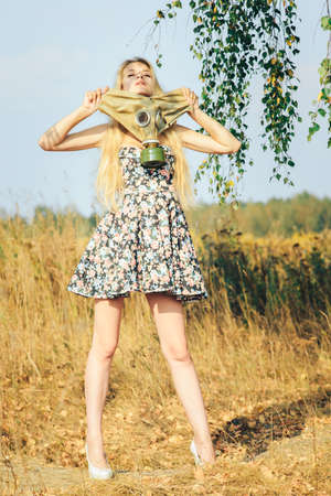 A girl in a dress walking in nature wears a gas mask. The concept of environmental pollution, viruses, and epidemics.の写真素材