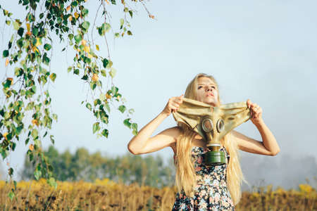 A girl in a dress walking in nature wears a gas mask. The concept of environmental pollution, viruses, and epidemics.の写真素材
