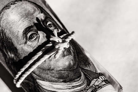 a bundle of hundred-dollar bills with a portrait of Benjamin Franklin, twisted and tied with a rope.の写真素材