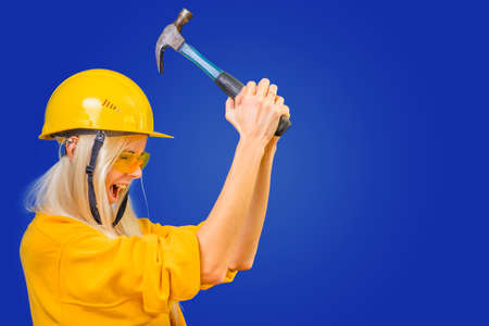 Carpenter girl with a tool and a helmet on her head on a blue background.の写真素材