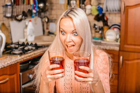 A girl in the kitchen with colored juices in glasses chooses which one to drink.の写真素材
