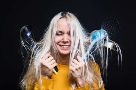 A young girl with disheveled hair holds kitchen tools, arrives terrified of not being able to cook anything. The concept of a young housewife.の写真素材