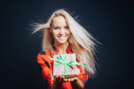 Happy, smiling girl holding a box with a festive bow in which a gift.